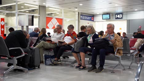 Pareja-De-Ancianos-Sentados-En-Las-Zonas-De-Embarque-Del-Aeropuerto-Mientras-Esperan-La-Lectura-De-Su-Vuelo,-París,-Francia