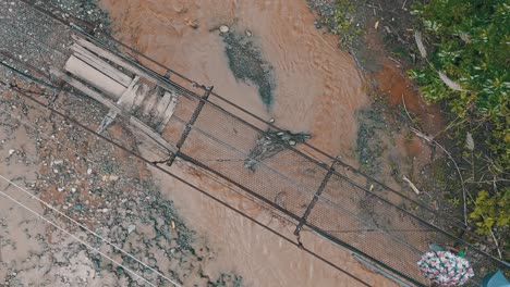 Rural-residence-crossing-a-old-rusty-temporary-bridge-over-the-flooded-river-during-rain