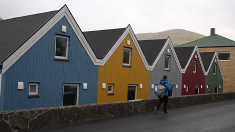 Man-walking-along-the-colorful-wooden-cottages-in-Sorvagur,-Vagar,-Faroe-Islands