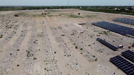 Jambur-solar-PV-power-plant-project-site-under-construction-aerial-left-panorama-revealing-vast-empty-dusty-land-and-equipment