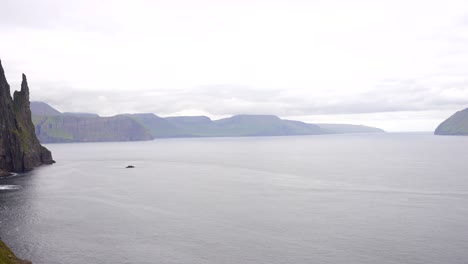 Pan-across-Trollkonufingur-to-Koltur-sheer-cliffs-of-the-Faroe-Islands-on-a-cloudy-day