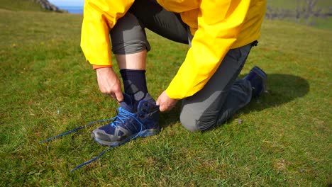 Medium-view-of-man-cleaning-off-sock-and-putting-on-hiking-boats-on-grassy-field