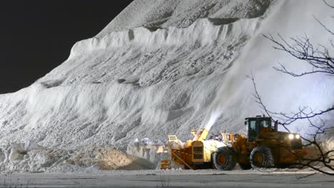 Huge-Pile-Of-Snow-At-Snow-Dump-With-Tractor-Snowblower-Working-At-Night