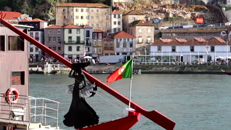 Portuguese-flag-at-the-stern-of-Rabelo-boat-next-to-a-woman-silhouette,-Porto