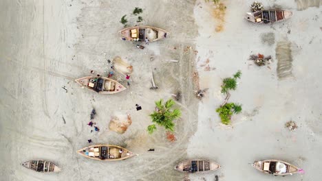 Top-View-Of-Fishermen-Repairing-Fishing-Nets-Next-Wooden-Canoes-In-Kuakata-Sea-Beach,-Bangladesh
