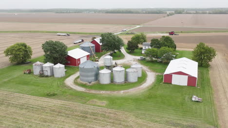 Aerial-View-of-Farm-with-Silos,-Barns,-and-Harvesting-Machinery-on-Expansive-Field