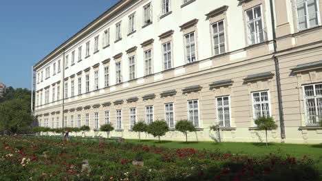Young-Woman-Walks-near-Facade-of-Mirabell-Palace-with-Gardens-on-a-Sunny-Day