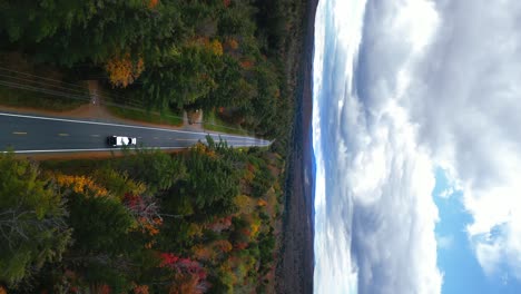Large-semi-truck-transporting-cargo-across-New-Hampshire-mountains-during-Fall-season,-vertical