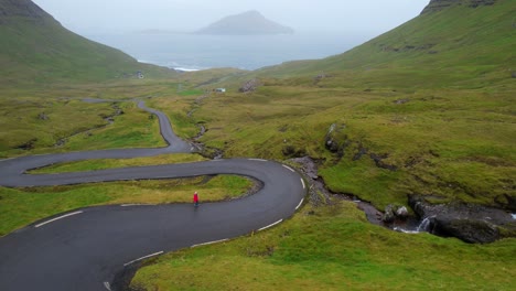 Solo-woman-walks-along-scenic-winding-road-of-Nordradalsskard,-Faroe-Islands