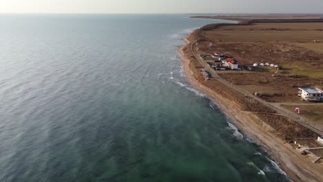 Cinematic-orbit-footage-of-Vama-Veche,-Romania's-coastal-gem,-in-a-breathtaking-aerial-view-over-the-Black-Sea-and-the-virgin-shore-being-hit-by-foamy-waves-at-sunrise