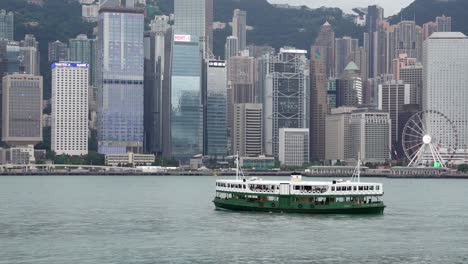 Star-ferry-sailing-through-the-harbour-with-the-view-of-skyline-buildings-under-gray,-Hazy-sky-due-to-air-pollution,-Hong-Kong,-China