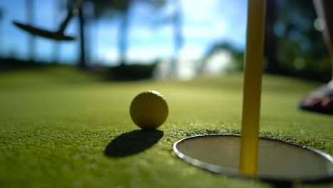 Mini-Golf-yellow-ball-with-a-bat-near-the-hole-at-sunset