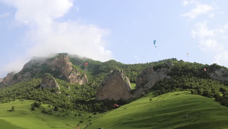 Paragliding-pilots-fly-paragliders-among-clouds-and-green-mountains.