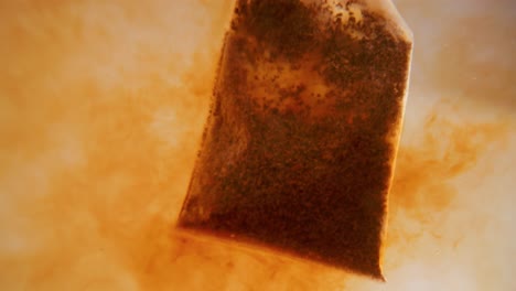 Close-up-of-tea-bag-diffusing-in-a-clear-glass.-Macro-slow-motion-shot-of-the-process-of-brewing-herbal.