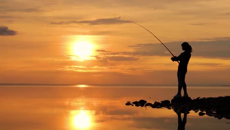 Woman-fishing-on-Fishing-rod-spinning-at-sunset-background.