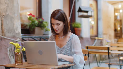 Woman-working-online-distant-job-with-laptop-in-city-cafe-or-restaurant-browsing-website-chatting