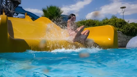 Descent-from-the-waterslide-on-holiday-aqua-park.-Slow-motion-on-a-water-slide-family-vacation,-a-woman-in-a-bikini-descends-from-the-slide-into-a-pool-of-blue-water-splashing-water-drops.