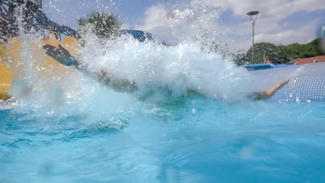 Descent-from-the-waterslide-on-holiday-aqua-park.-Slow-motion-on-a-water-slide-family-vacation,-a-woman-in-a-bikini-descends-from-the-slide-into-a-pool-of-blue-water-splashing-water-drops.