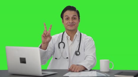 Fröhlicher-Indischer-Arzt-Zeigt-Siegeszeichen-Auf-Grünem-Bildschirm