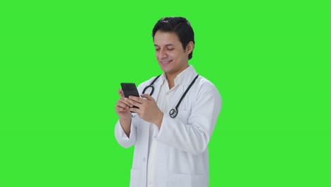 Fröhlicher-Indischer-Arzt,-Der-Auf-Dem-Grünen-Bildschirm-Des-Telefons-Chattet