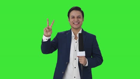 Cheerful-Indian-reporter-showing-victory-sign-Green-screen