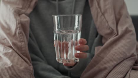 Close-up-of-woman-holding-glass-with-pill-dissolving-in-water.