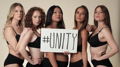 Portrait-of-group-of--serious-women-in-underwear-standing-in-the-studio-and-holding-a-banner.