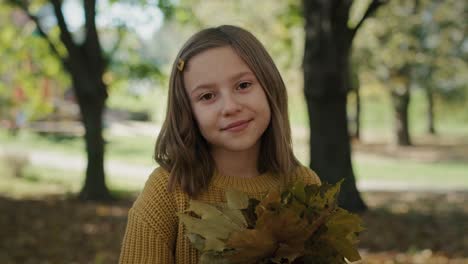 Portrait-of-smiling-little-girl-with-bouquet-of-autumn's-leaves.