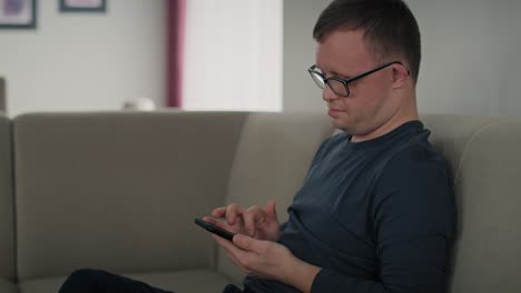 Man-with-down-syndrome-using-mobile-phone-at-home-while-sitting-on-sofa