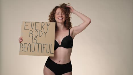 Cheerful-caucasian-red-head-woman-in-underwear-in-the-studio-holding-a-banner.