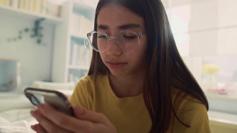 Pensive-caucasian-teenage-girl-browsing-phone-in-her-room
