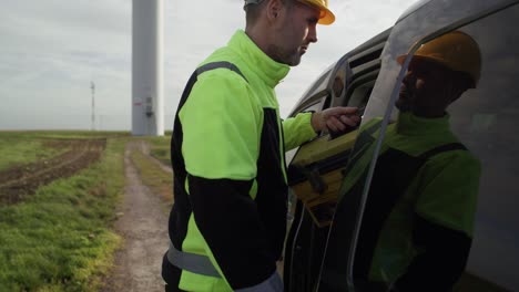 Caucasian-male-professional-came-to-field-with-windmill-with-tool-box.
