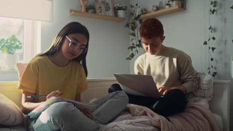 Zwei-Kaukasische-Teenager-Sitzen-Auf-Dem-Bett-Und-Lernen-Gemeinsam-Aus-Büchern-Und-Einem-Laptop