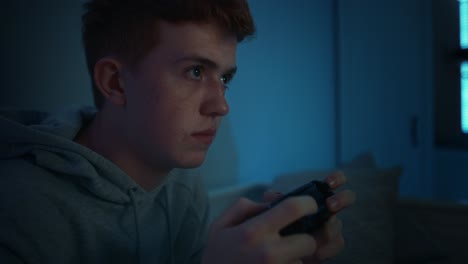 Focus-caucasian-teenage-boy-playing-on-game-controller-at-night