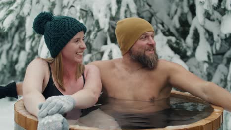Caucasian-couple-sitting-in-wooden-barrel-with-frozen-water.