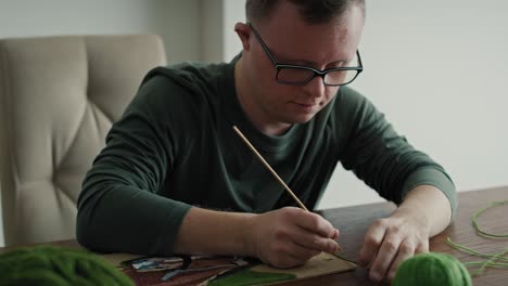Close-up-of-adult-caucasian-man-with-down-syndrome-making-a-craft-at-home