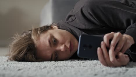 Caucasian-sad-woman-using-mobile-phone-and-lying-down-on-carpet.