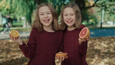 Two-caucasian-sisters-holding-oranges-and-grapefruit-on-their-eyes-in-autumn.