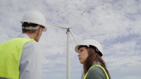 Two-caucasian-engineers-standing-on-wind-turbine-field-and-discussing-over-documents.