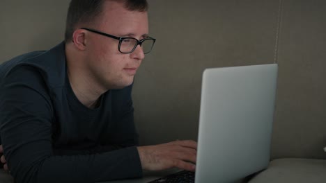 Man-with-down-syndrome-using-laptop-at-home-while-lying-on-sofa.