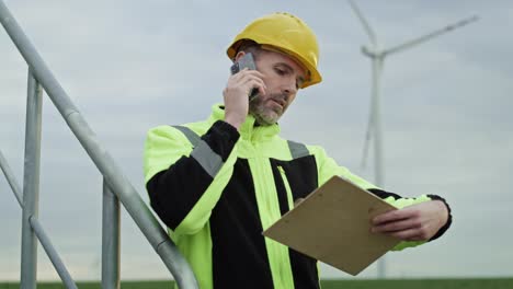 Caucasian-professional-man-standing-on-wind-turbine-field-and-talking-by-mobile-phone.