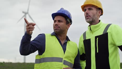 Caucasian-and-latin-male-engineers-standing-on-wind-turbine-field-and-discussing-together.