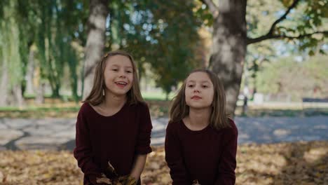 Portrait-of-smiling-little-girls-which-throwing-up-autumn-leaves.