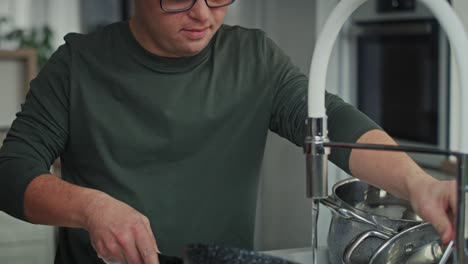 Tilt-up-of-adult-caucasian-man-with-down-syndrome-washing-dishes-at-home