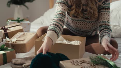 Caucasian-woman-sitting-on-bed-and-packing-Christmas-gift-in-bedroom