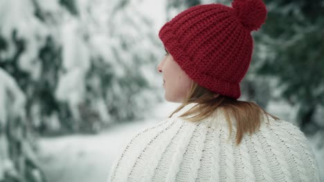 Caucasian-woman-wearing-red-hat-walking-in-snowing-forest.