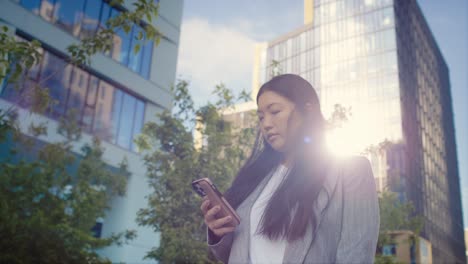 Business-Chinese-woman-walking-in-the-city-and-using-phone