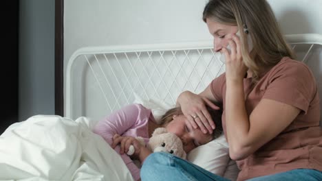 Mother-calling-a-doctor-while-her-daughter-lying-ill-in-bed