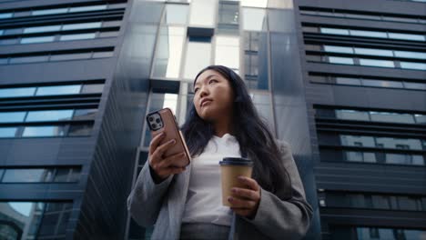 Vista-De-ángulo-Bajo-De-Una-Mujer-China-De-Negocios-Parada-En-La-Calle-De-La-Ciudad-Y-Enviando-Mensajes-De-Texto-Al-Teléfono