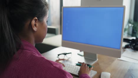 Rückansicht-Einer-Frau-Mit-Gemischter-Abstammung,-Die-Am-Computer-Auf-Blauem-Bildschirm-Arbeitet